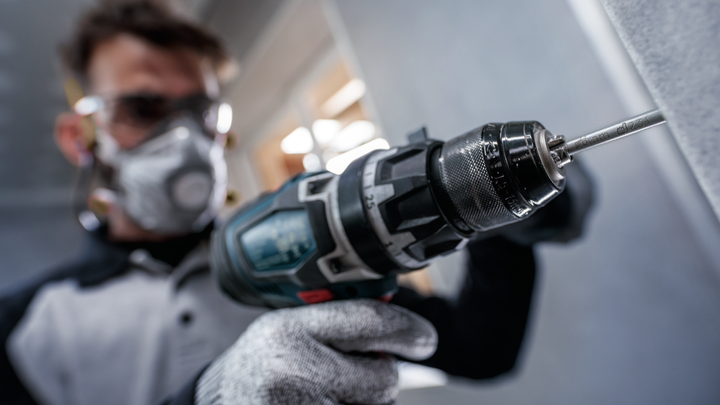 Una persona che indossa un equipaggiamento di sicurezza fora un muro con un utensile elettrico.