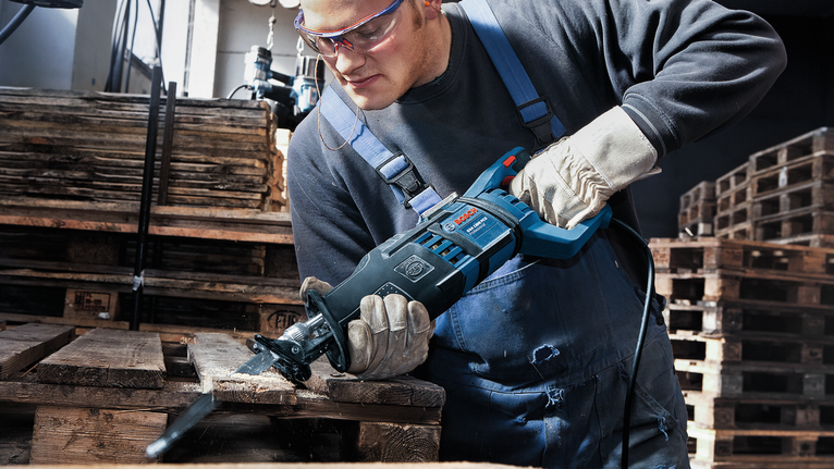 Una persona che indossa dispositivi di sicurezza utilizza una sega alternativa per tagliare i pallet di legno.