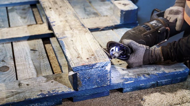 Una persona che indossa un equipaggiamento di sicurezza usa un seghetto alternativo per tagliare un pallet di legno.