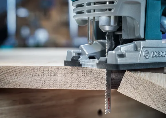 Un seghetto alternativo taglia una linea curva precisa attraverso una tavola di legno.