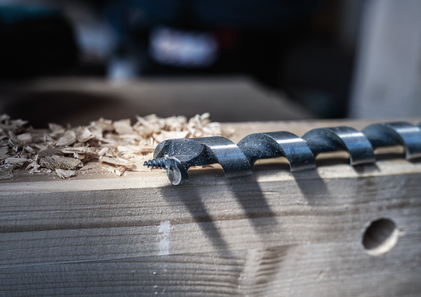 Grande punta da trapano con trucioli di legno su una trave di legno liscia.