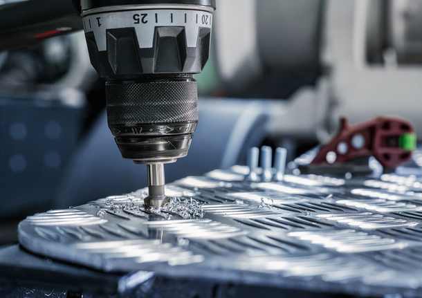 Trapano che realizza fori precisi in un pezzo di metallo, circondati da trucioli metallici.
