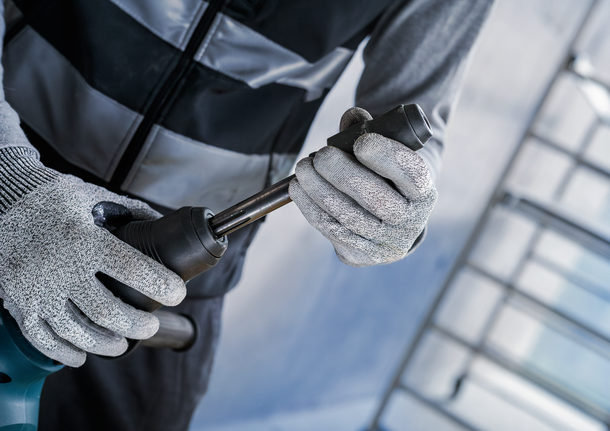 Una persona che indossa un equipaggiamento di sicurezza fissa una punta metallica a un utensile elettrico.