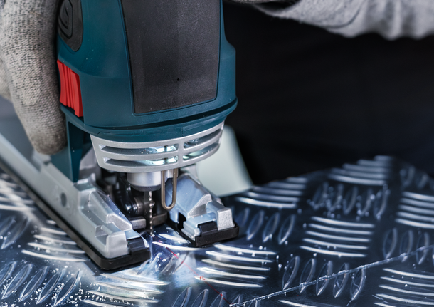 Una persona che indossa un equipaggiamento di sicurezza usa un seghetto alternativo per tagliare il metallo decorato.