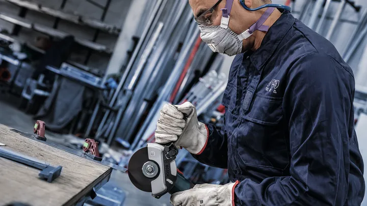 Una persona che indossa un equipaggiamento di sicurezza taglia il metallo utilizzando una smerigliatrice angolare.