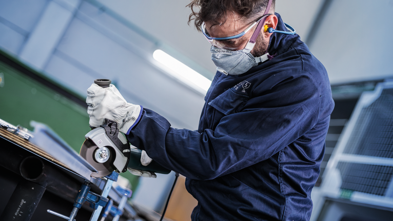 Una persona che indossa un equipaggiamento di sicurezza utilizza una smerigliatrice angolare per tagliare il metallo.