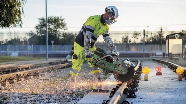 Una persona che indossa un equipaggiamento di sicurezza taglia i binari di una ferrovia con una sega elettrica.