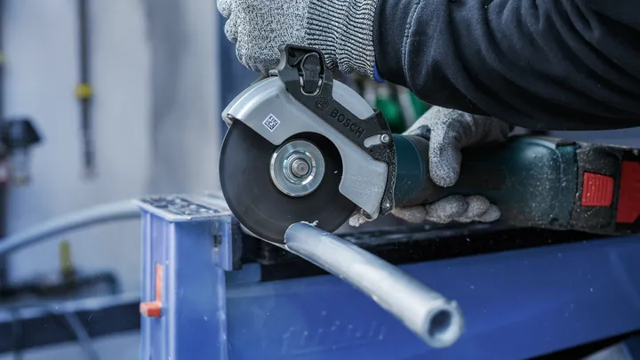 Una persona che indossa un equipaggiamento di sicurezza taglia un tubo di metallo con una smerigliatrice angolare.