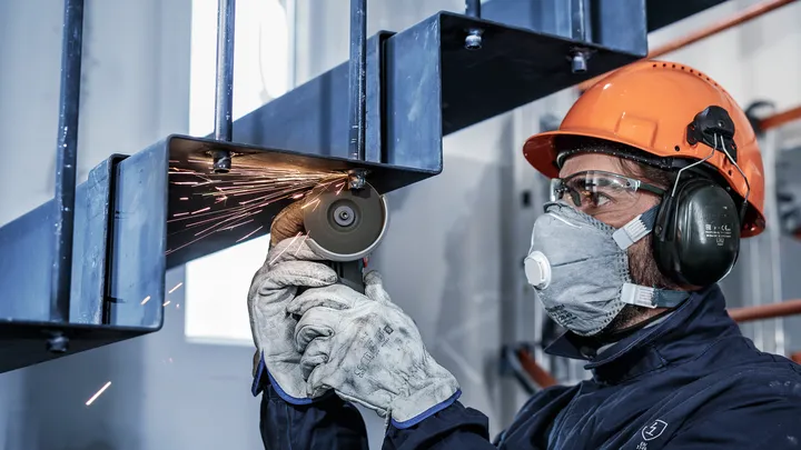 Una persona che indossa dispositivi di sicurezza taglia una scala metallica con una smerigliatrice.