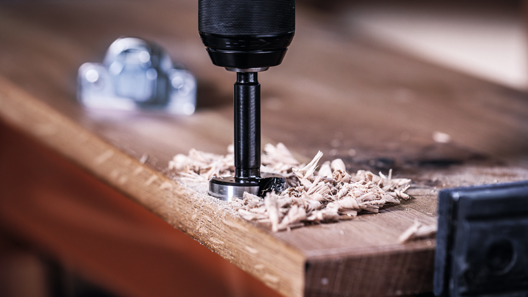 Un trapano con una sega a tazza crea un foro in una tavola di legno.