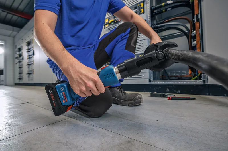 Una persona che indossa un equipaggiamento di sicurezza utilizza un utensile da taglio idraulico senza fili su un cavo spesso.