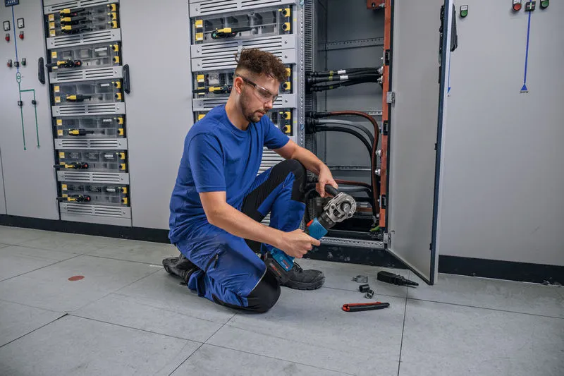 Una persona che indossa un equipaggiamento di sicurezza crimpa un cavo utilizzando un utensile idraulico senza fili.