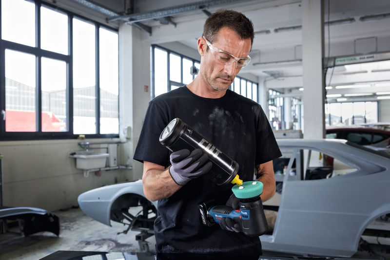 Una persona che indossa un equipaggiamento di sicurezza applica il lucidante su una lucidatrice elettrica in un'officina.