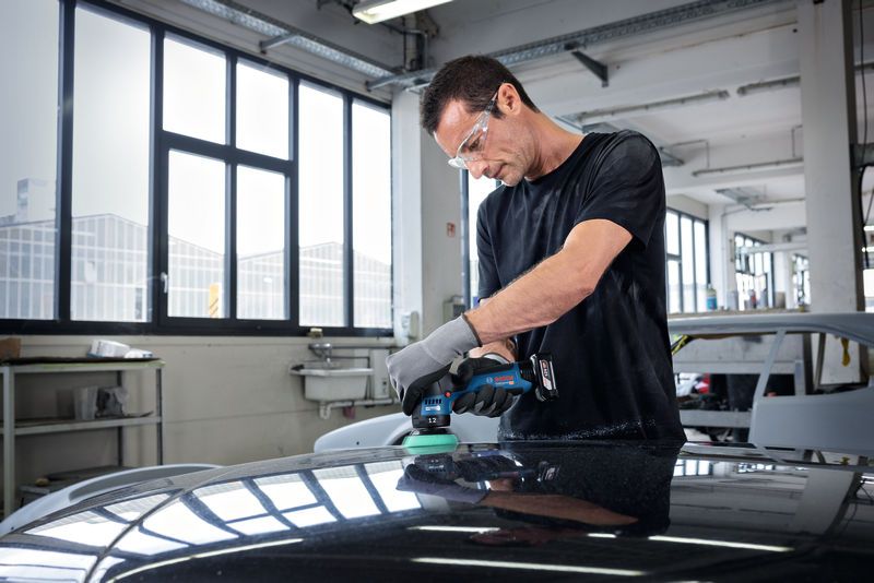 Una persona che indossa dispositivi di sicurezza lucida il cofano di un'auto in un'officina.