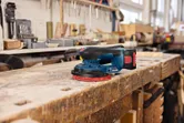 Levigatrice orbitale casuale a batteria appoggiata su un banco da lavoro in legno usurato in un'officina.