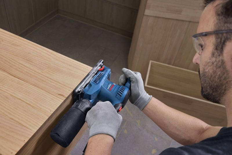 Persona che indossa dispositivi di sicurezza mentre leviga il legno con una levigatrice orbitale.