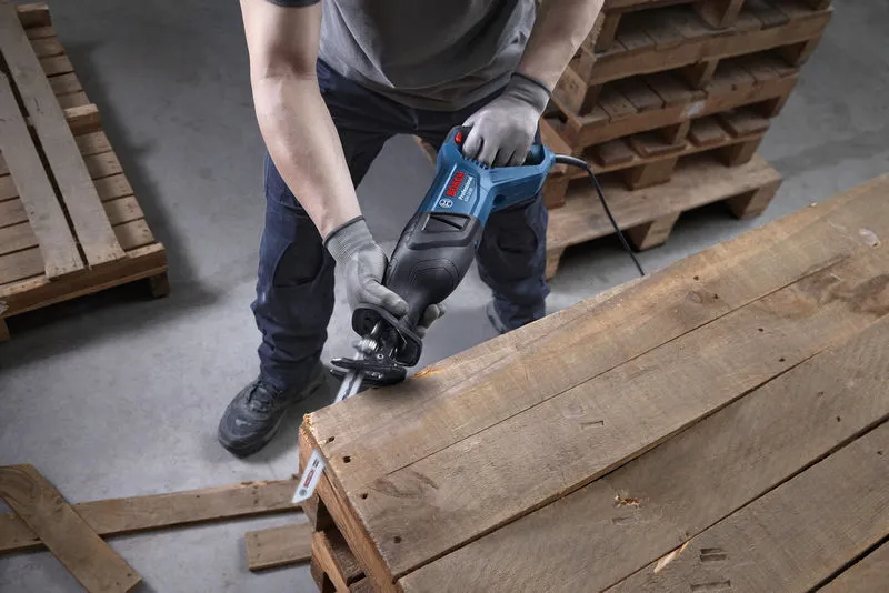 Una persona che indossa un equipaggiamento di sicurezza utilizza un seghetto alternativo per tagliare un pallet di legno.