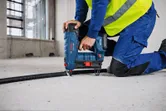Una persona che indossa dispositivi di protezione individuale fissa un cavo al cemento utilizzando una chiodatrice pneumatica per cemento.