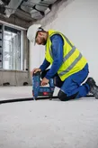 Una persona che indossa un equipaggiamento di sicurezza installa un cavo con una chiodatrice a batteria in un cantiere edile.