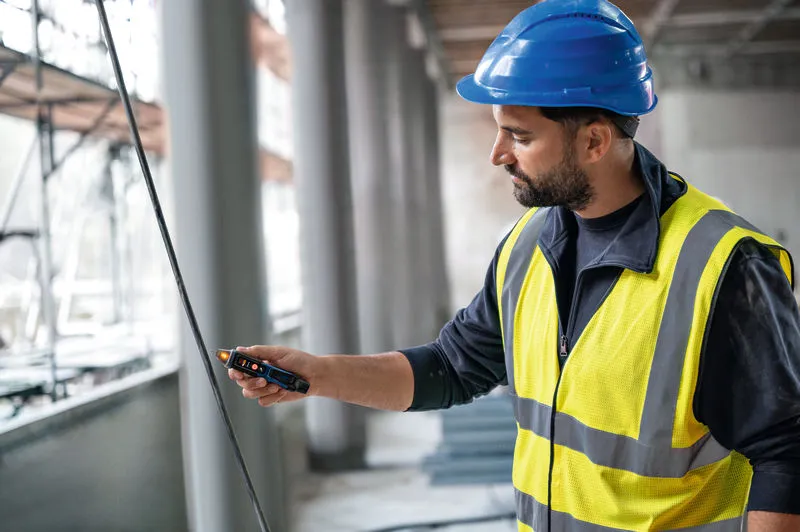 Una persona che indossa un equipaggiamento di sicurezza testa un cavo con un misuratore di tensione senza contatto.