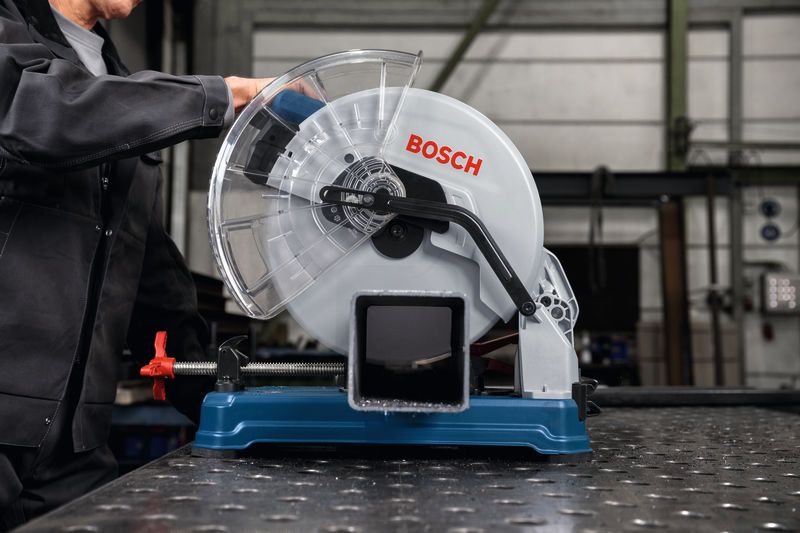 Una persona che indossa un equipaggiamento di sicurezza aziona una sega troncatrice per metalli su un tubo di acciaio.