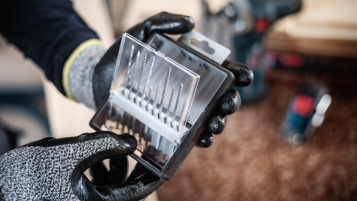 Una persona che indossa un equipaggiamento di sicurezza tiene in mano un set di punte da trapano in una custodia di plastica.