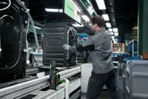 Una persona che indossa un equipaggiamento di sicurezza assembla un elettrodomestico su una linea di produzione in fabbrica con un controller intelligente.
