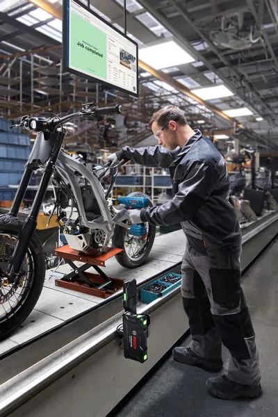 Una persona che indossa l'equipaggiamento di sicurezza assembla il telaio di una motocicletta in una postazione di lavoro in fabbrica.