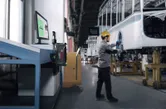 Una persona che indossa un equipaggiamento di sicurezza utilizza un elettroutensile per assemblare il telaio di un veicolo in una fabbrica.