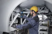 Una persona che indossa un equipaggiamento di sicurezza utilizza una chiave a impulsi su un telaio metallico.