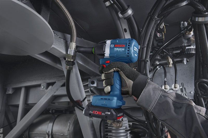 Una persona che indossa dispositivi di sicurezza utilizza una chiave a impulsi a batteria su macchinari industriali.