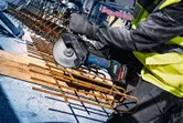 Una persona che indossa dispositivi di sicurezza taglia barre d'acciaio con una smerigliatrice angolare a batteria.