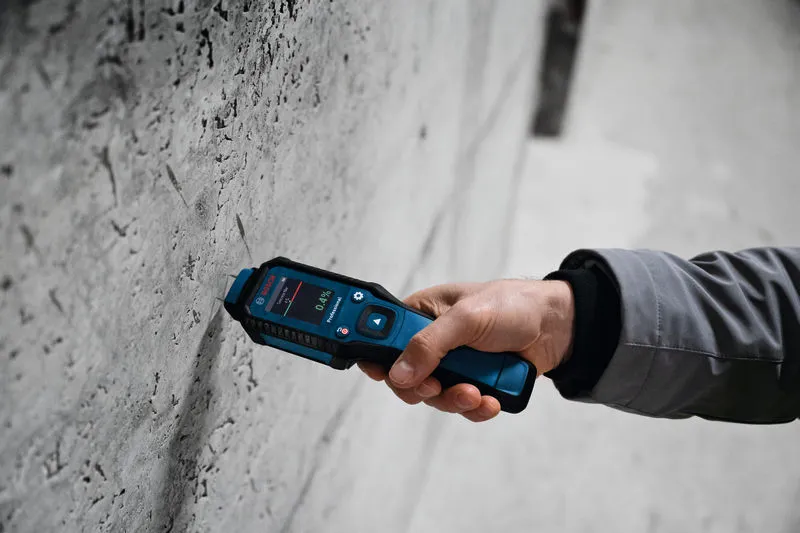 Una persona utilizza un misuratore di umidità per controllare i livelli di umidità in un muro di cemento.