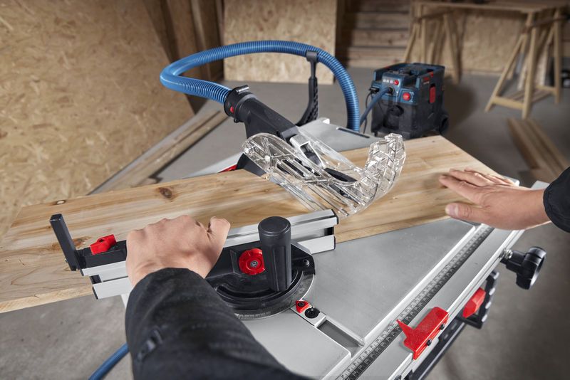 Una persona guida una tavola di legno attraverso una sega circolare in un'officina.