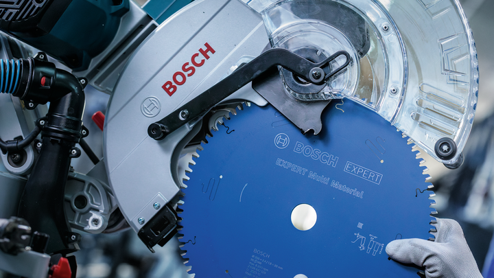 Una persona che indossa dispositivi di sicurezza installa una lama blu su una sega troncatrice.