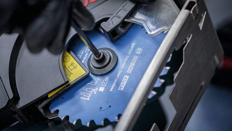 Una persona che indossa un equipaggiamento di sicurezza stringe la lama di una sega circolare con un utensile manuale.