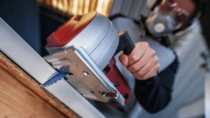 Una persona che indossa un equipaggiamento di sicurezza taglia una tavola con una sega circolare.