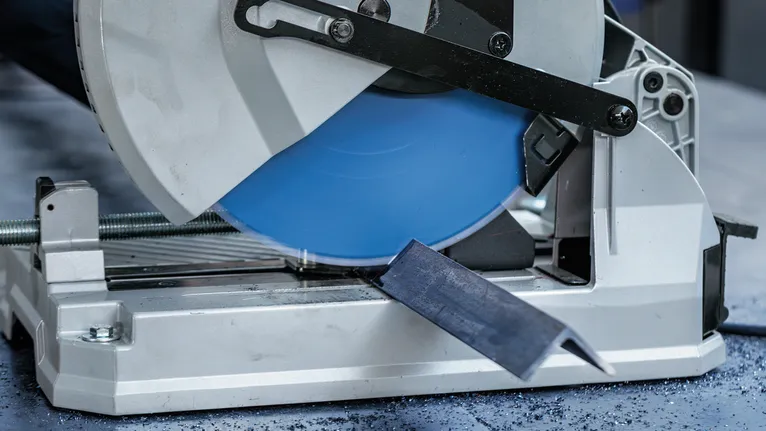 Una sega circolare per metalli taglia una barra d'acciaio sul pavimento di un'officina.