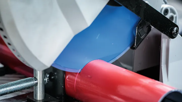 Sega circolare che taglia un tubo di metallo rosso in un'officina.