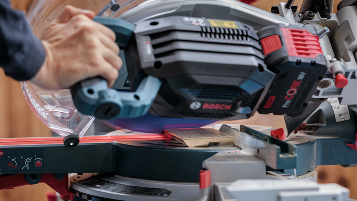 Persona che guida una sega troncatrice scorrevole attraverso una tavola di legno.