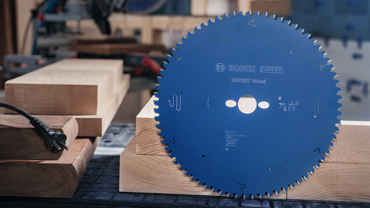 Una grande lama di sega circolare appoggiata verticalmente su un banco da lavoro in legno in una falegnameria.