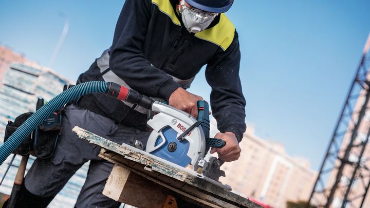 Una persona che indossa dispositivi di sicurezza utilizza una sega circolare per tagliare la legna in un cantiere edile.