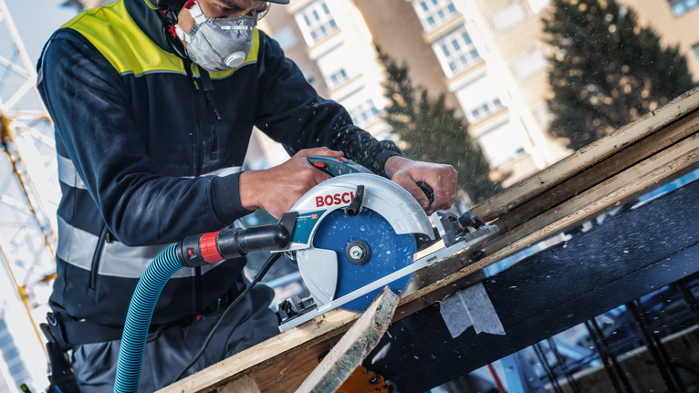 Una persona che indossa dispositivi di sicurezza taglia la legna con una sega circolare in un cantiere edile.