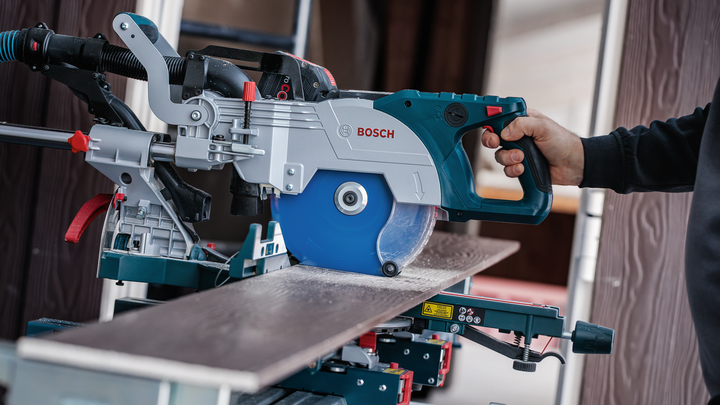 Una persona taglia un'asse di legno con una sega circolare su un banco da lavoro.