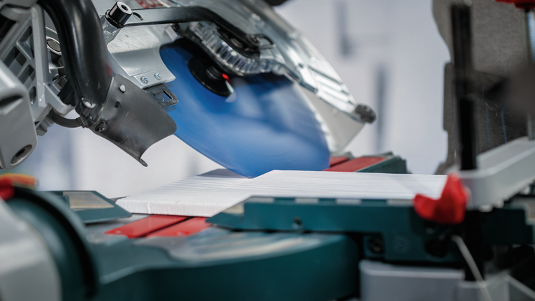 Sega circolare che taglia una tavola bianca su un supporto per sega troncatrice.