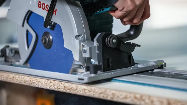 Una persona guida una sega circolare lungo un binario per tagliare una tavola di legno.