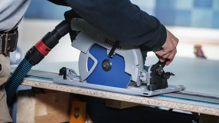 Una persona che indossa dispositivi di sicurezza guida una sega circolare lungo una tavola di legno.