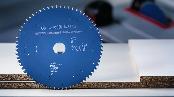 Lama di sega circolare esposta in verticale su un tavolo accanto a tavole di legno laminato.