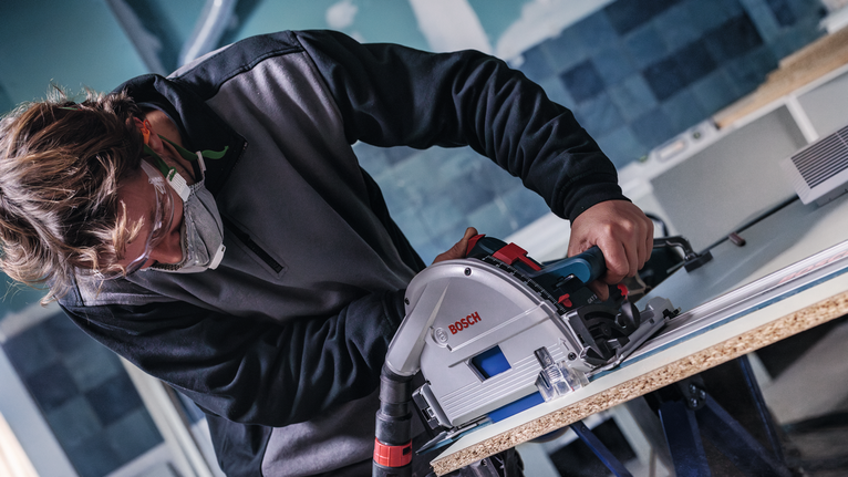 Una persona che indossa dispositivi di sicurezza taglia il legno laminato con una sega circolare.