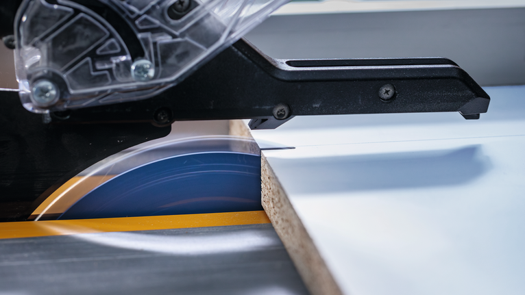 Sega circolare che taglia una tavola di legno laminata su un banco da lavoro.